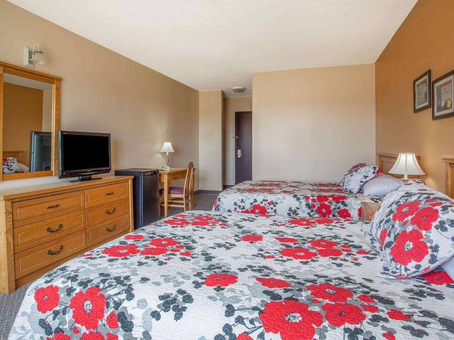 A hotel room with two beds, a wooden dresser, a television, and a desk with a chair.