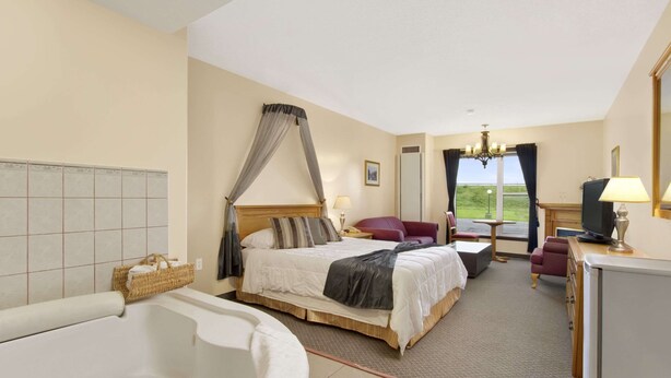 A hotel room with a large bed, a sitting area with a chair and table, a TV, and a bathtub. - Knights Inn Woodstock (Jacksonville)