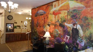 A hotel lobby with a large mural, a chandelier, a reception desk, and seating areas. - Knights Inn Woodstock (Jacksonville)