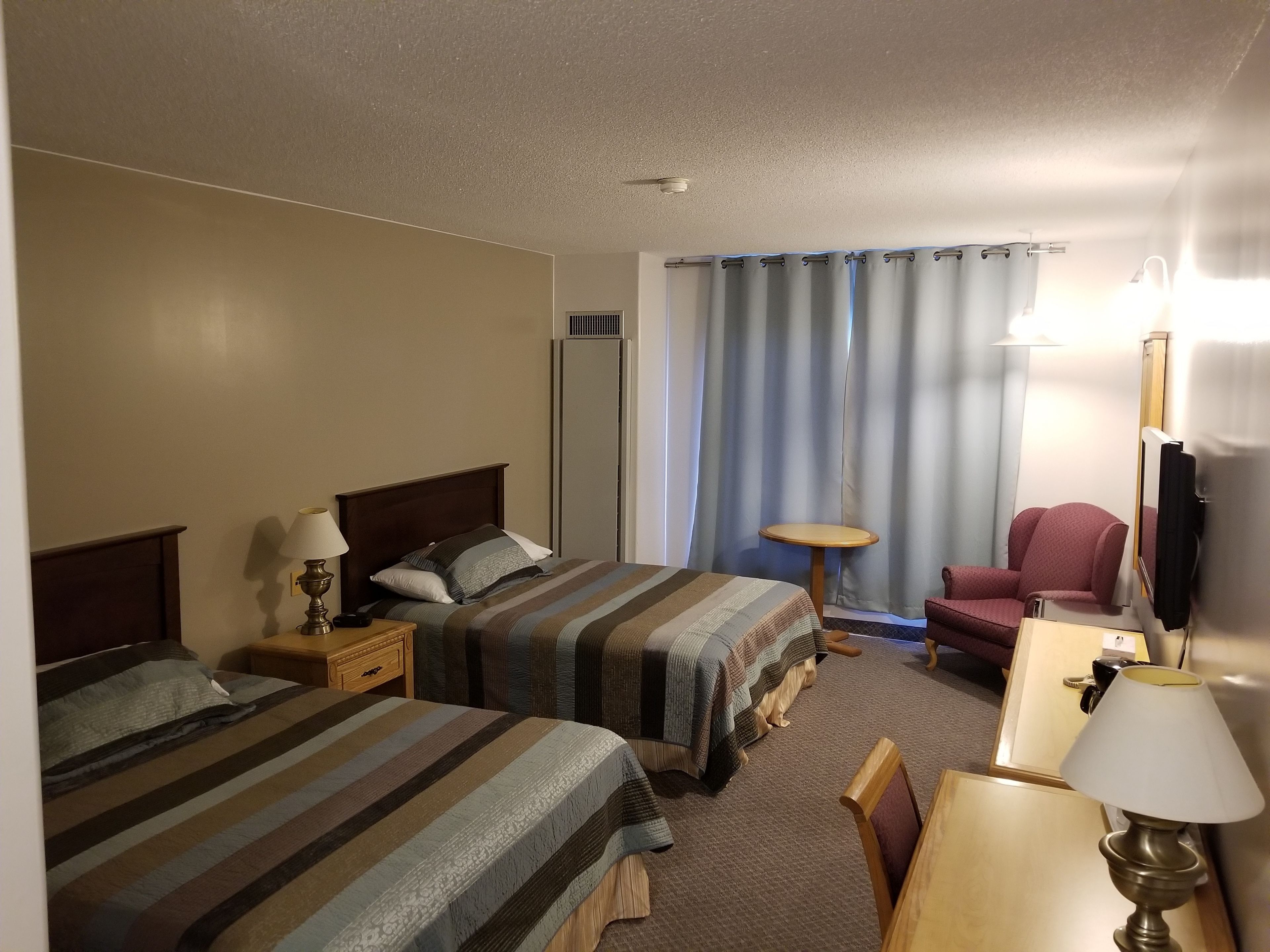 Habitación de hotel con dos camas, un escritorio, una silla, un espejo y una ventana con cortinas.