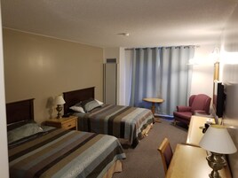 Habitación de hotel con dos camas, un escritorio, una silla, un espejo y una ventana con cortinas.