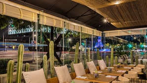 Een buitenterras met houten tafels en stoelen, omringd door cactussen.