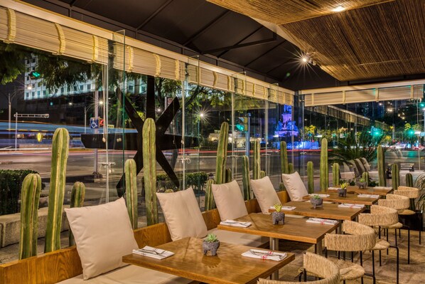 Un área de comedor al aire libre con mesas y sillas de madera, rodeada de cactus.
