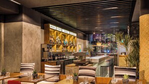 Een restaurant met houten tafels en rode stoelen, een bar met flessenrekken, en uitzicht op de stad 's nachts.