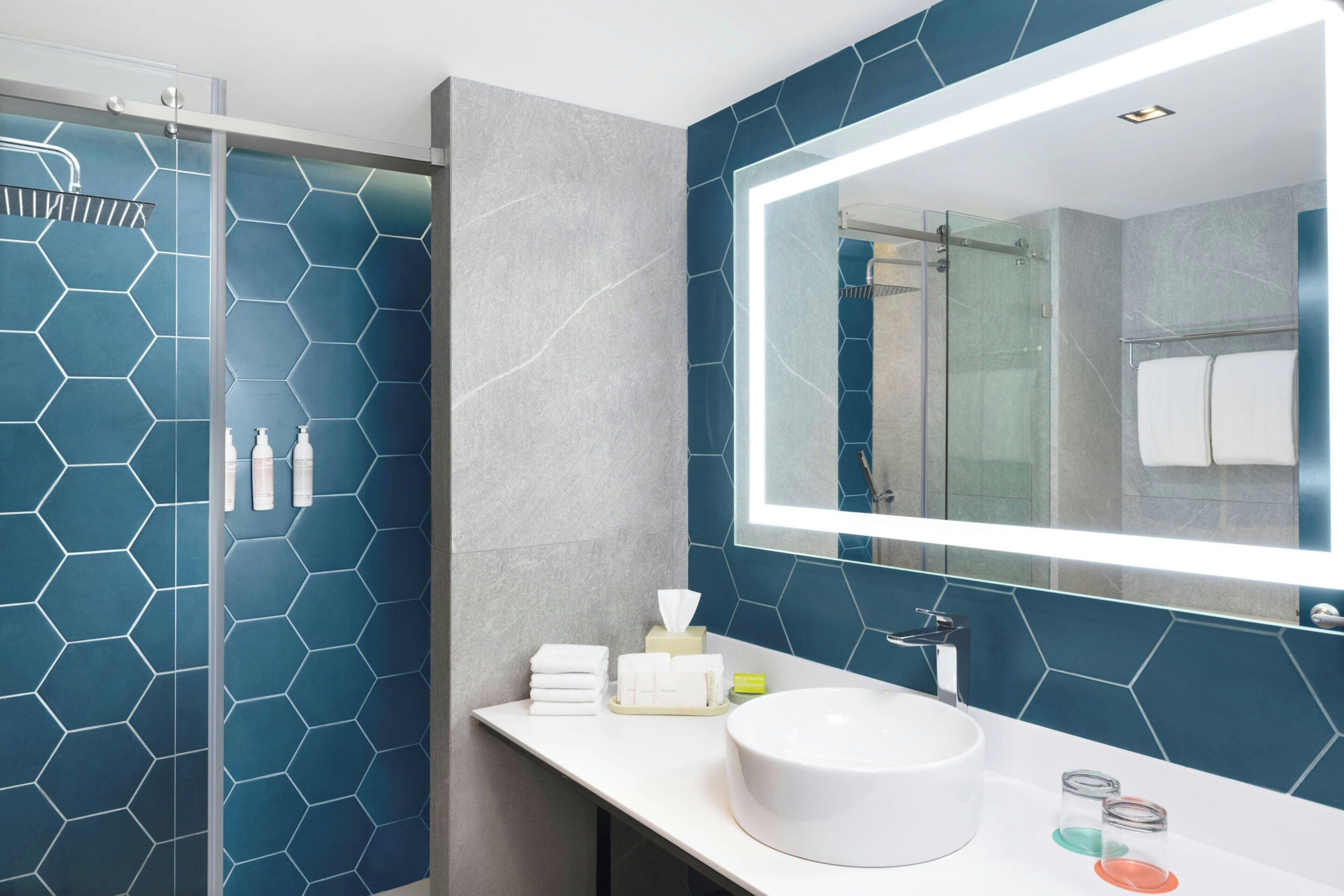 A modern bathroom with a glass shower enclosure, a large mirror, and a white sink.