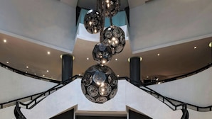 Een statige lobby met een centrale trap, zwarte leuningen en een zwart tapijt dat naar de bovenverdiepingen leidt.