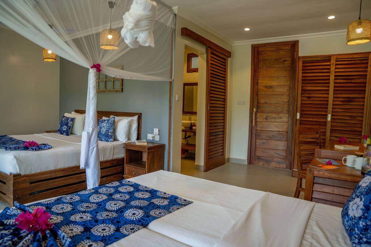 A room with two beds, a canopy bed, wooden furniture, and a bathroom visible through an open door.