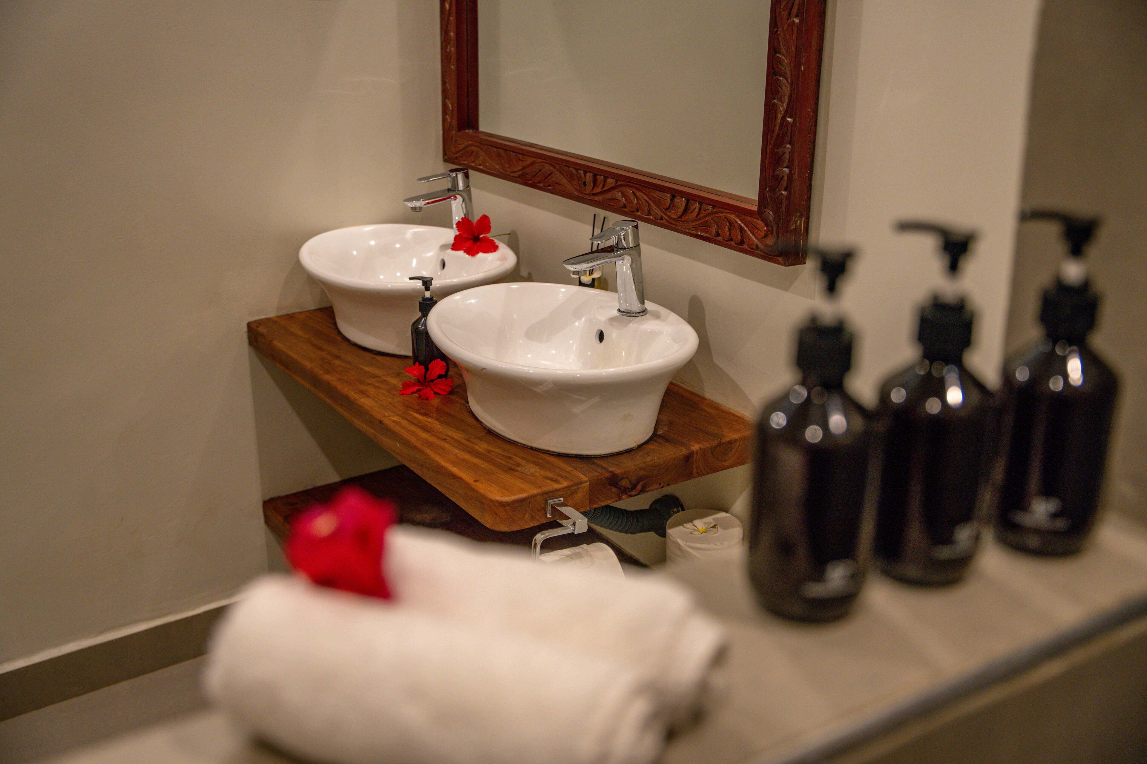 A bathroom with two sinks, a wooden shelf, and toiletries.