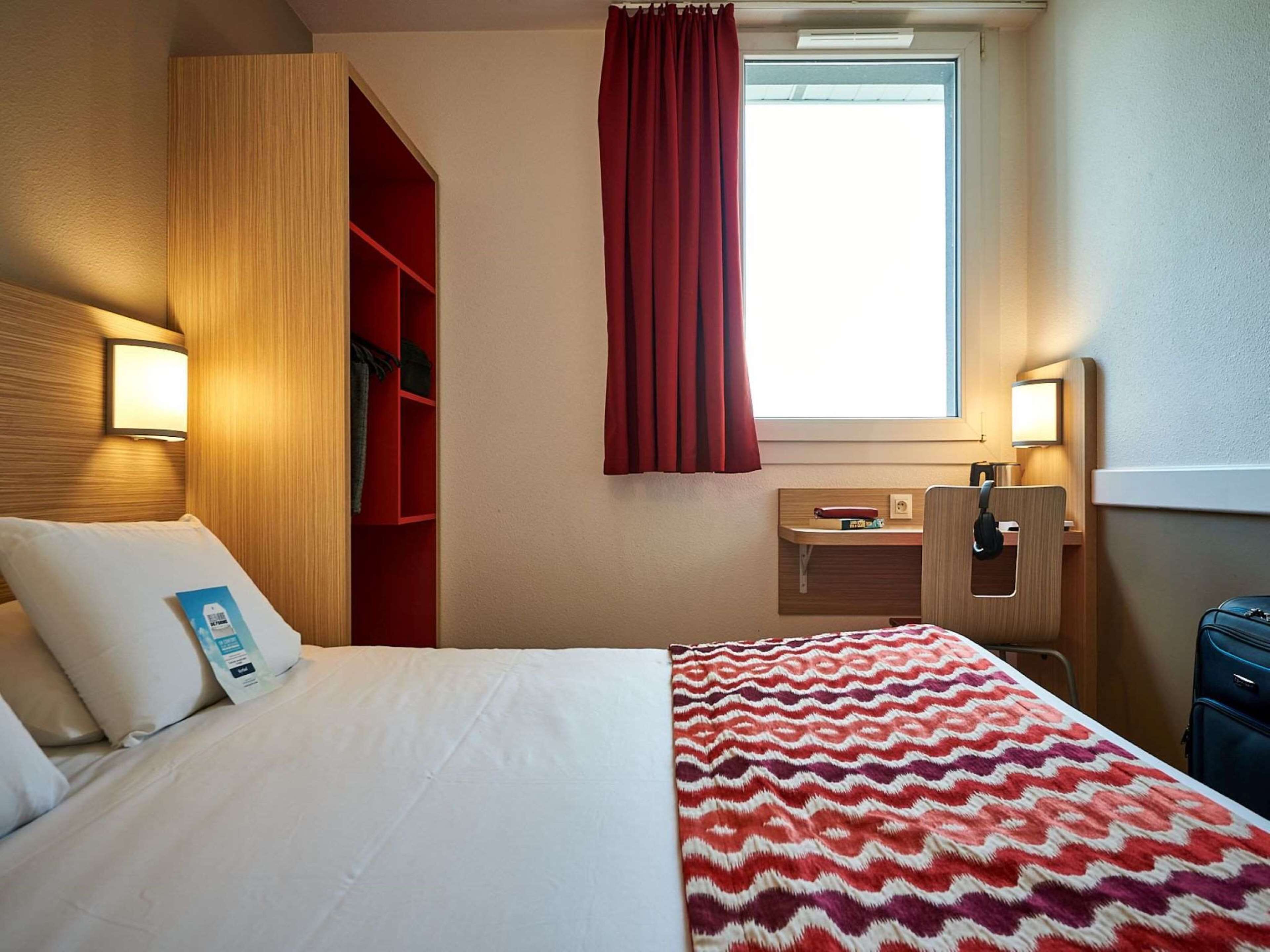 A hotel room with a bed, a desk, a wardrobe, and a window with curtains.