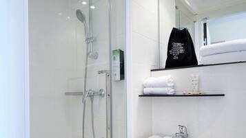 A modern bathroom with a glass-enclosed shower, a white sink, and shelves with towels and toiletries.