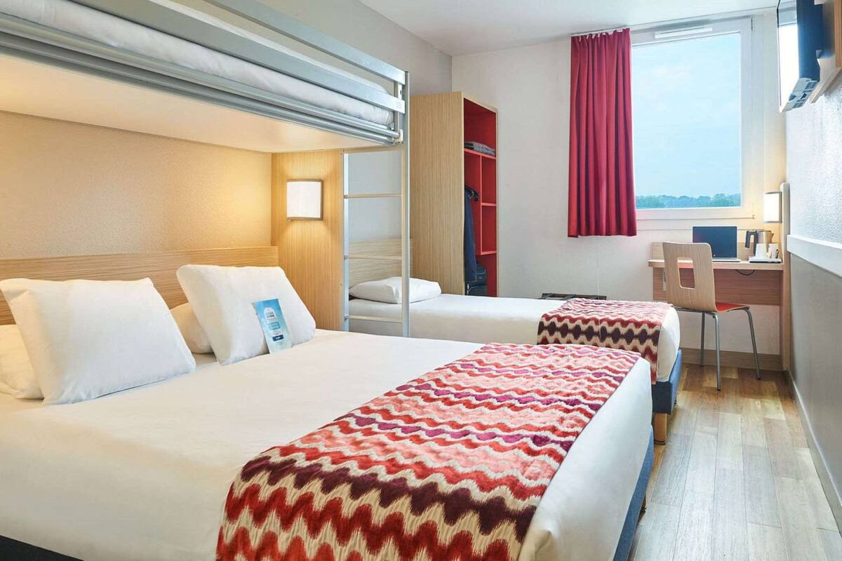 A hotel room with two beds, a desk, a chair, a TV, and a window with curtains.