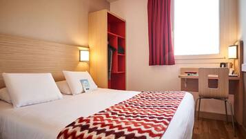 Ein Hotelzimmer mit einem Bett, einem Schreibtisch, einem Stuhl, einem Kleiderschrank und einem fenster mit Vorhängen.