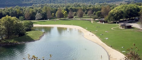 A lakeside park with a sandy beach, grassy areas, and a pond.