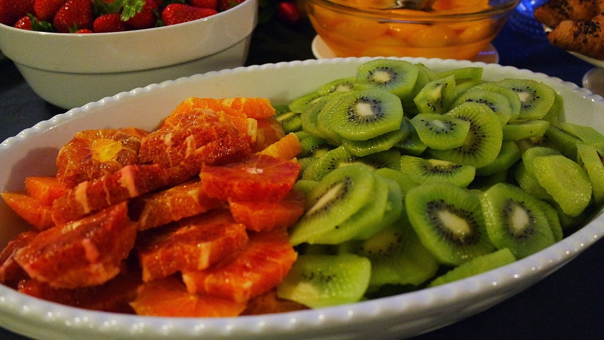 A bowl of sliced fruits including oranges and kiwi.