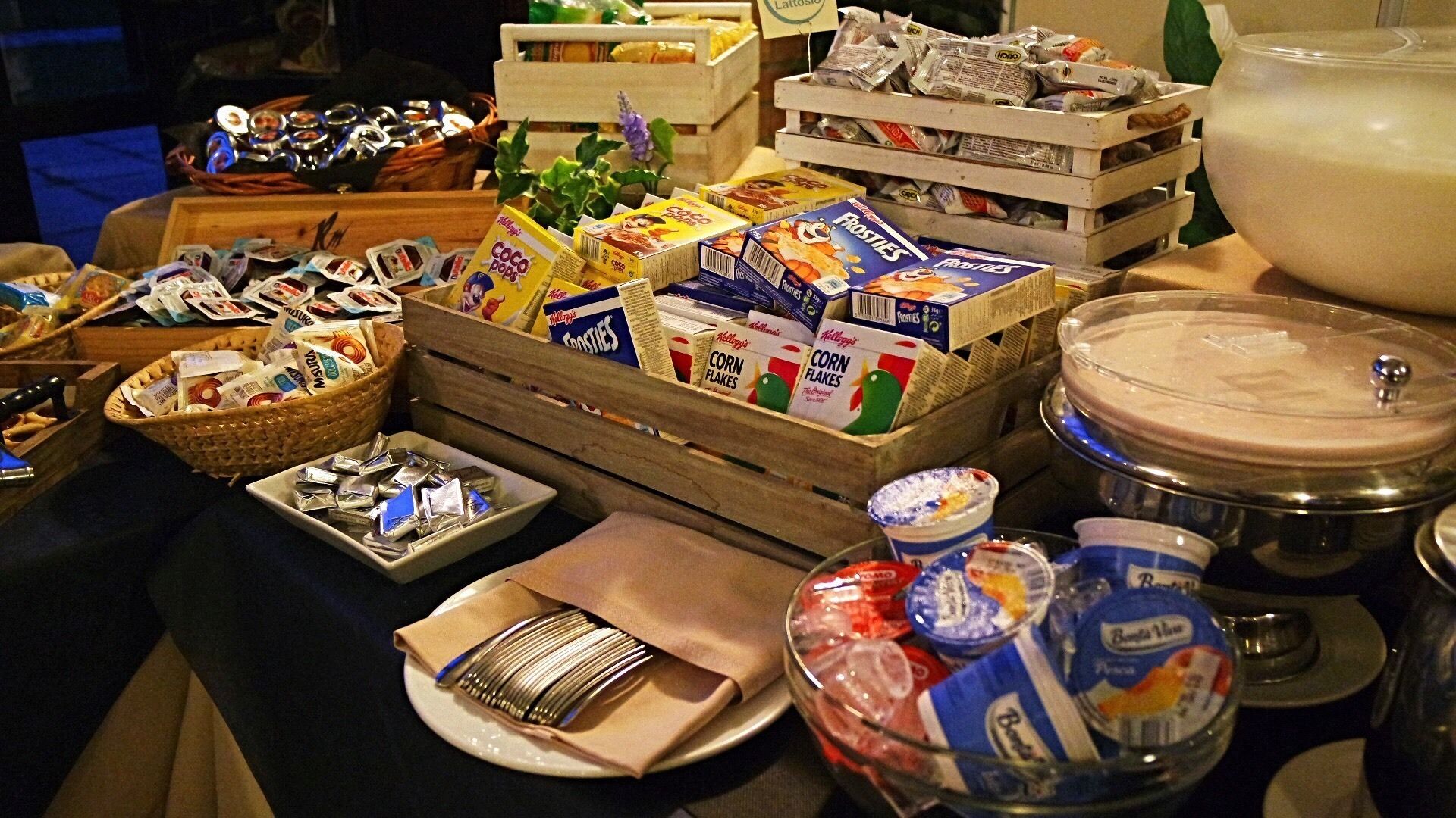 Een buffet met verschillende soorten eten, zoals cornflakes, snacks en een grote verpakking van een romige drank.