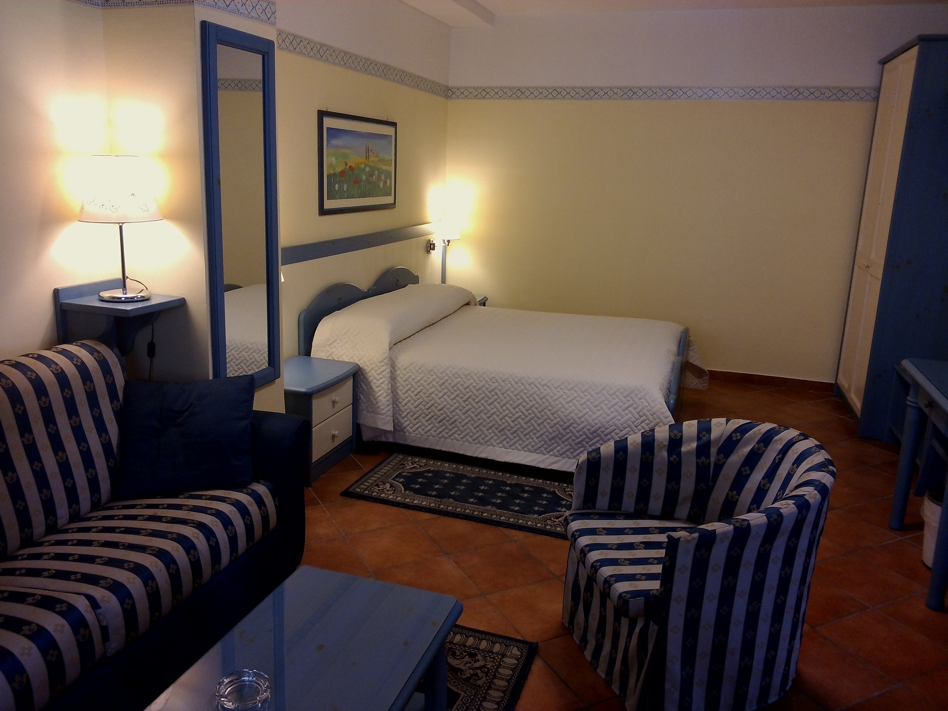 A bedroom with a bed, a nightstand, a lamp, a chair, and a small table.