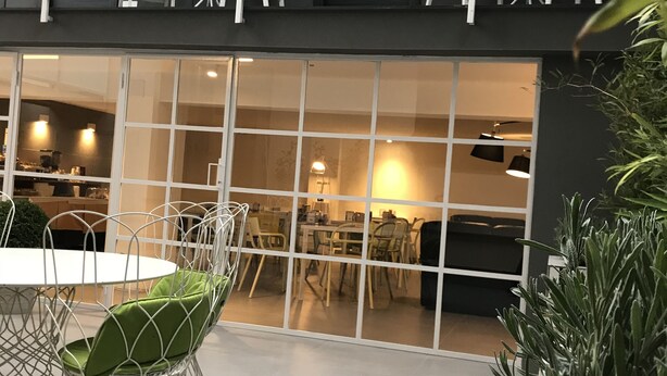 An outdoor dining area with a white table and chairs, a glass railing, and a view of the interior space. - Albergo del Pino (Cercola)