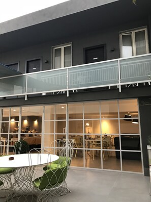 A modern building with a glass balcony and a dining area with green chairs and a white table. - Albergo del Pino (Cercola)