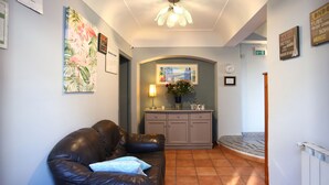 A living room with a leather sofa, a small table with a lamp, and a wall with a clock and framed pictures. - Albergo del Pino (Cercola)