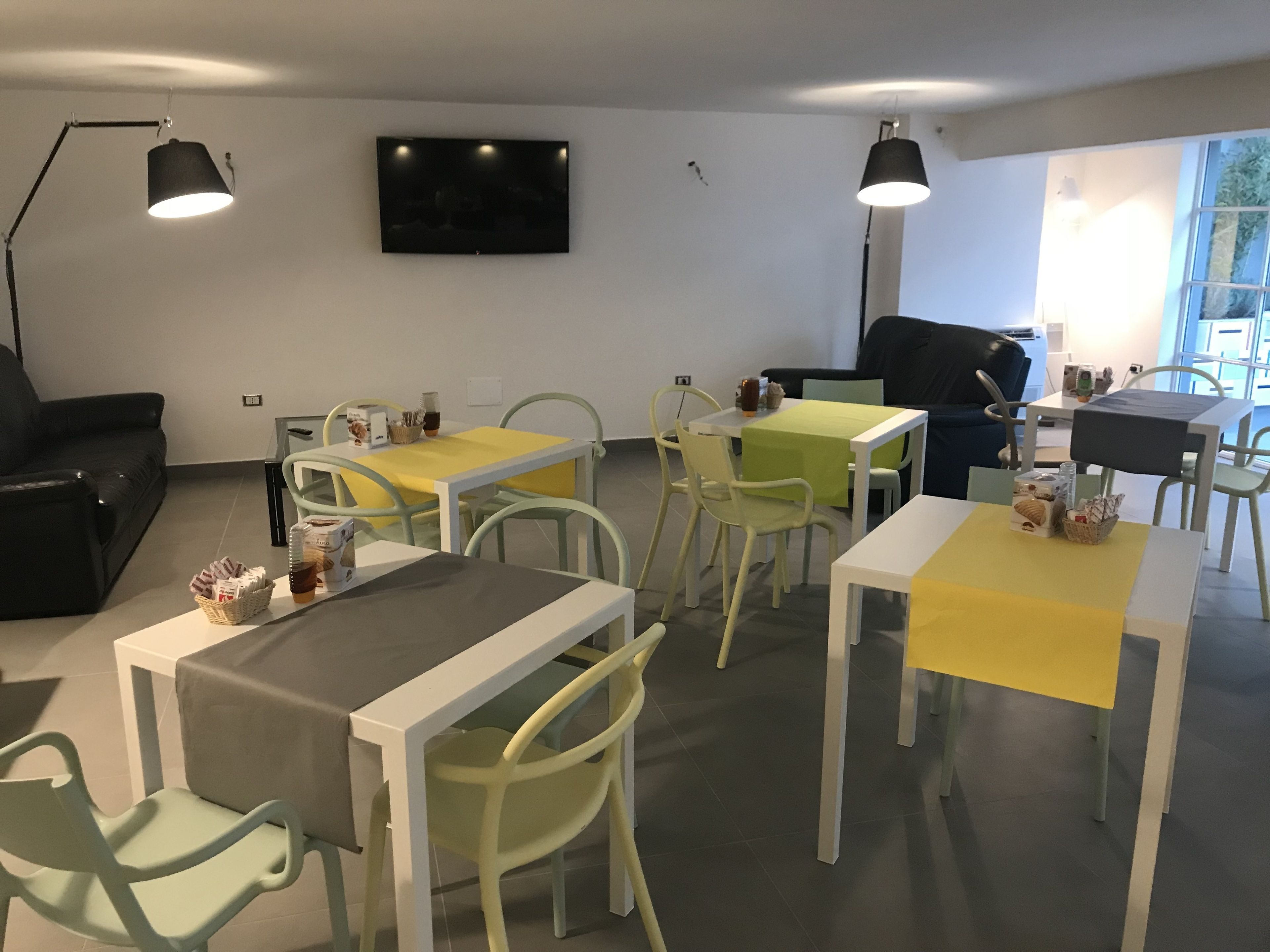 A modern dining area with tables and chairs, a flat-screen TV on the wall, and a window providing natural light.