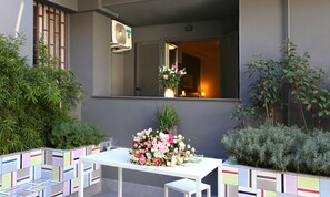 A small outdoor seating area with a white table and chairs, a floral arrangement, and a window with a view into the interior. - Albergo del Pino (Cercola)