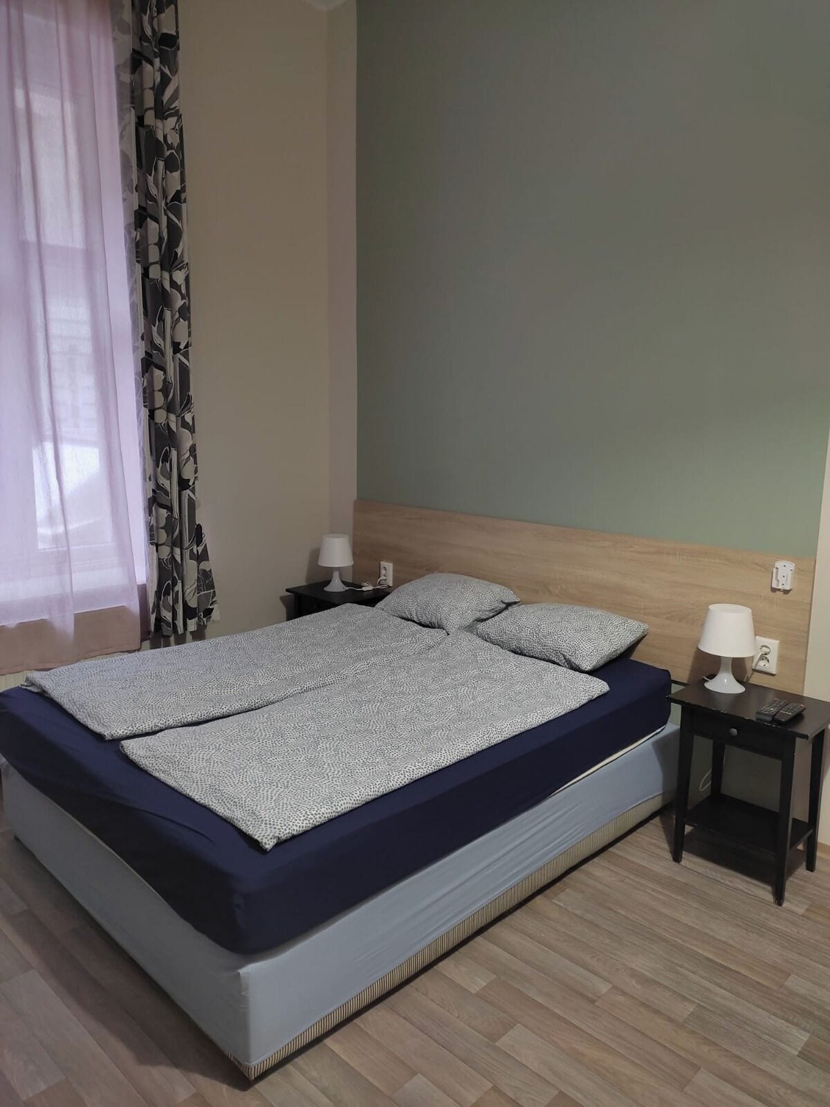 Une chambre à coucher avec un lit, deux tables de chevet, une commode et une fenêtre avec des rideaux.