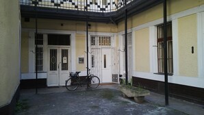 A courtyard with a bicycle, a planter with plants, and a white door with barred windows. - Downtown Apartments (Budapest)