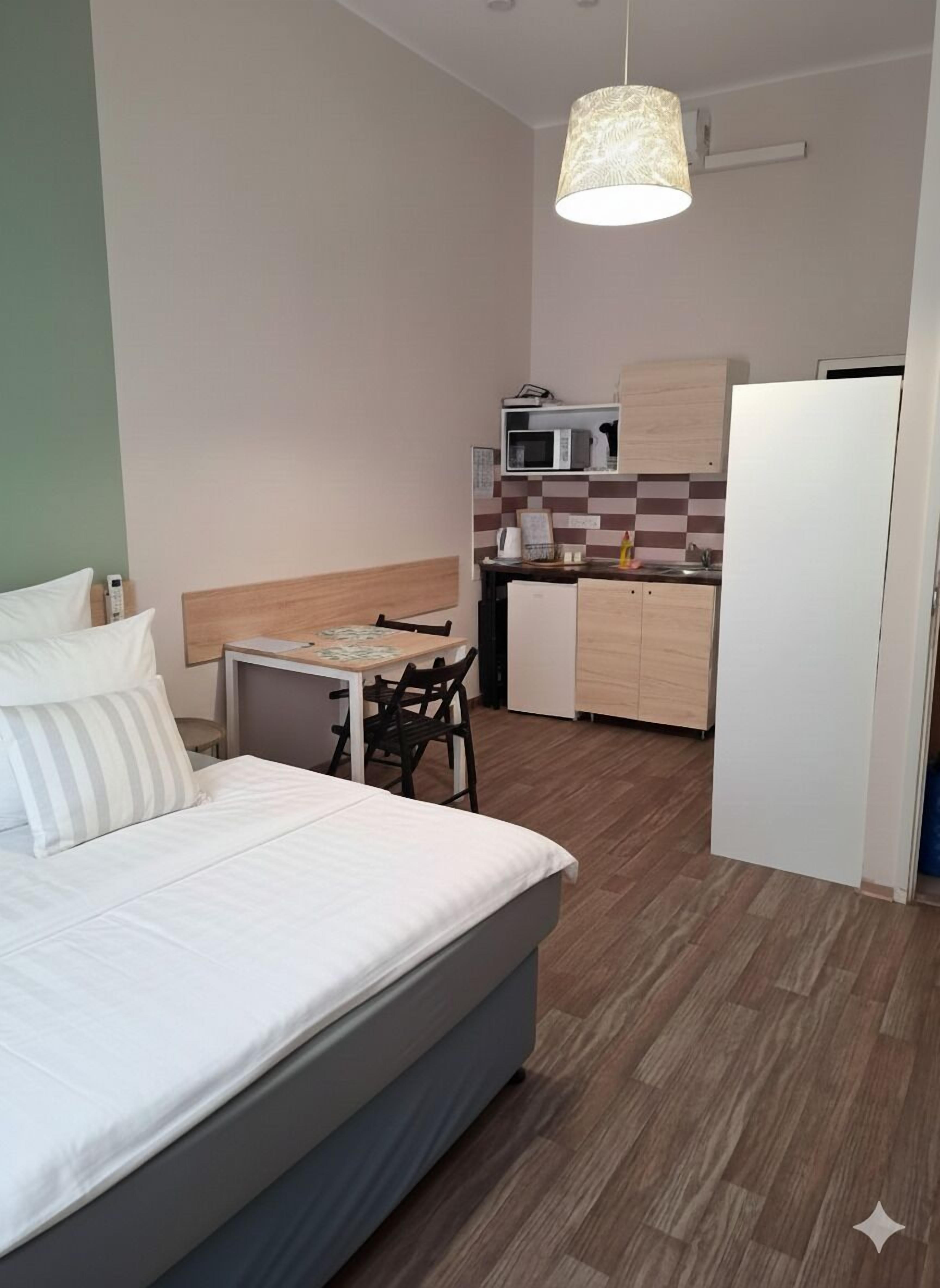 Une chambre d’hôtel de taille réduite, comprenant un lit, un petit bureau, une chaise, un four à micro-ondes, un réfrigérateur et un luminaire suspendu.