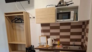 A compact kitchen with a microwave, sink, and small refrigerator. There is a wooden cabinet above the microwave and a wooden shelf unit to the left. - Downtown Apartments (Budapest)
