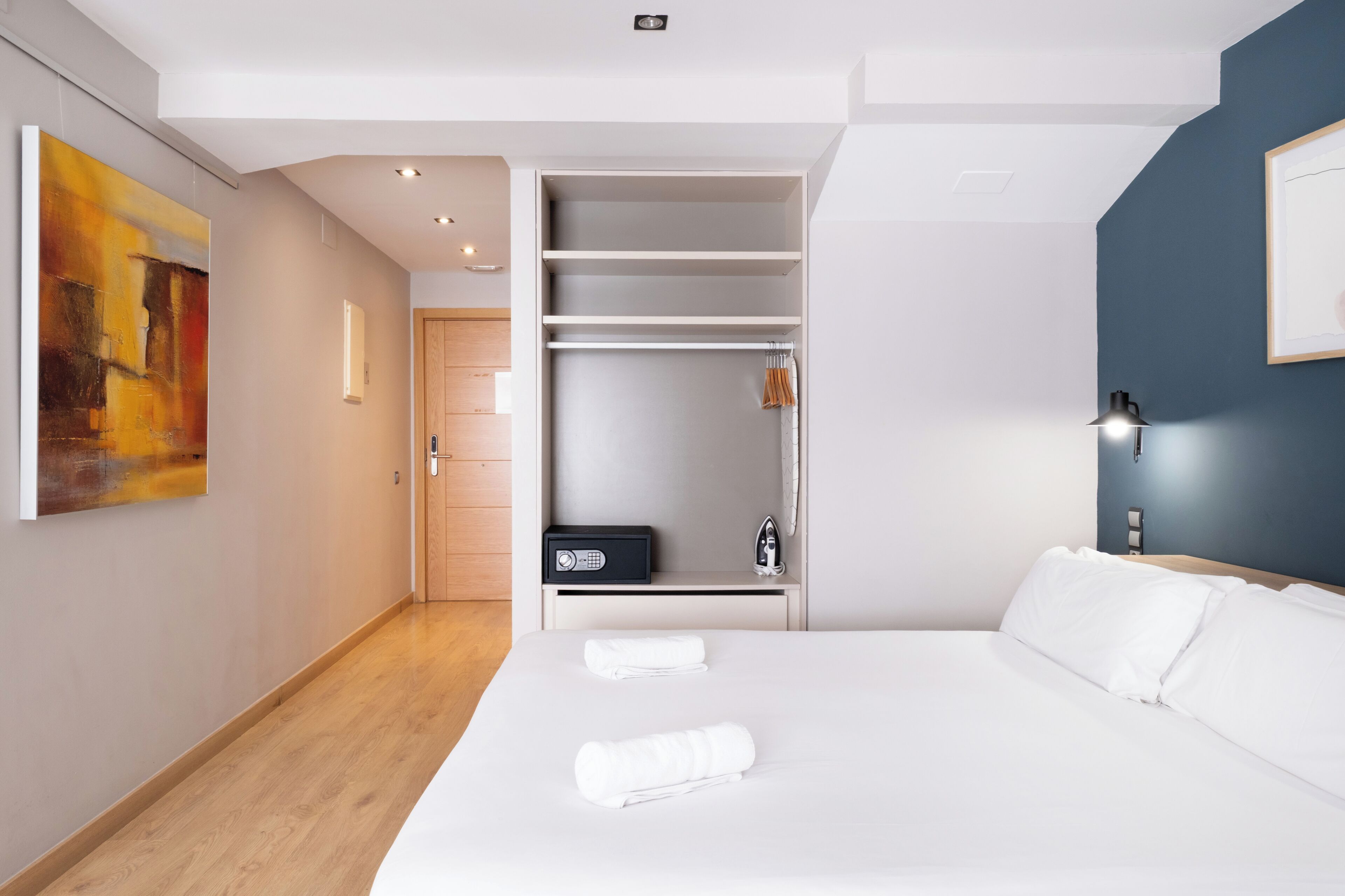 Une chambre d’hôtel moderne avec un grand lit, un dressing et un tableau au mur.