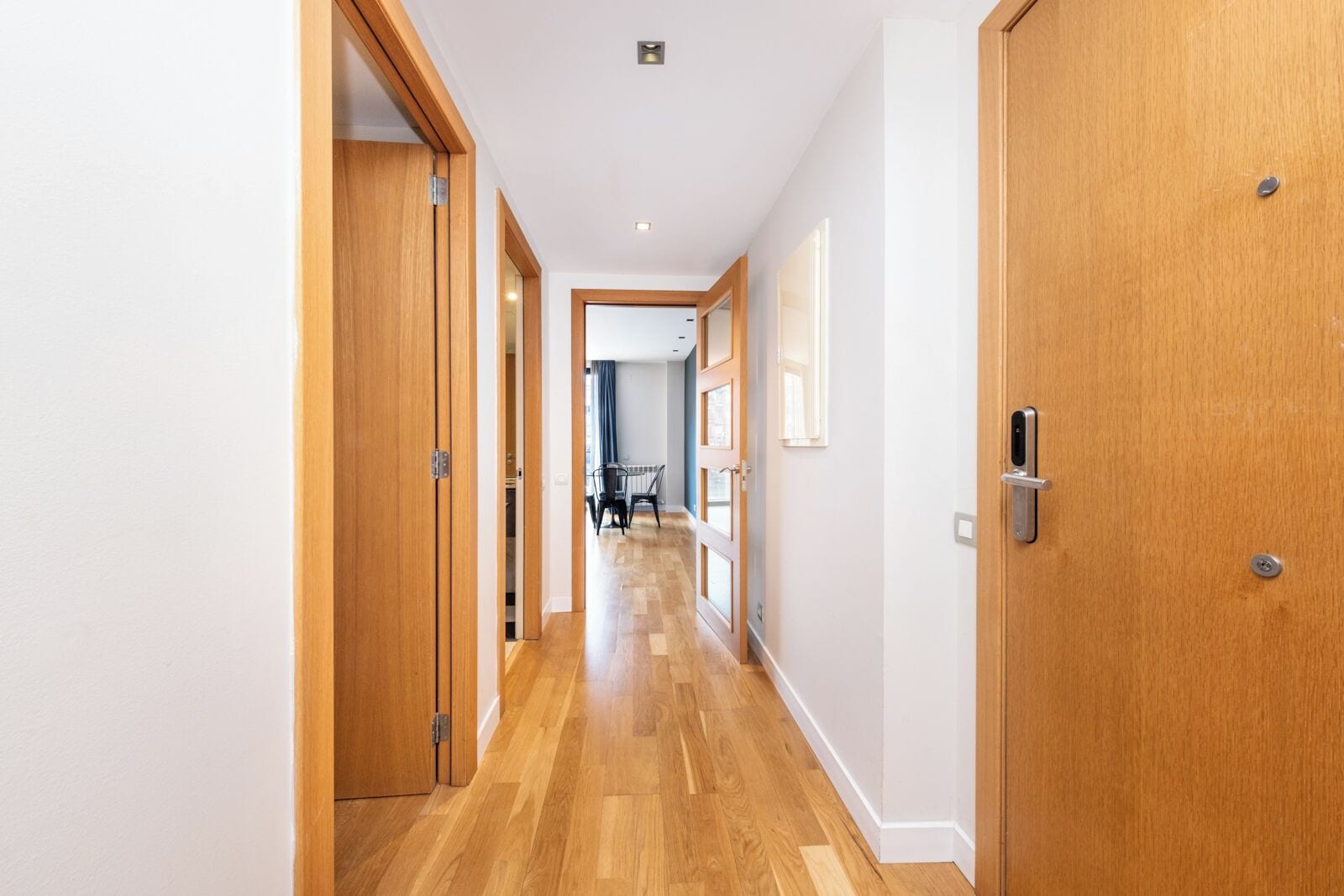 A hallway with wooden doors, a dining area in the background, and a ceiling light.
