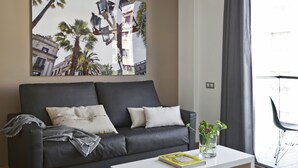 Una sala de estar moderna con un sofá de cuero oscuro, una mesa de centro blanca y un cuadro grande con una vista de la ciudad.