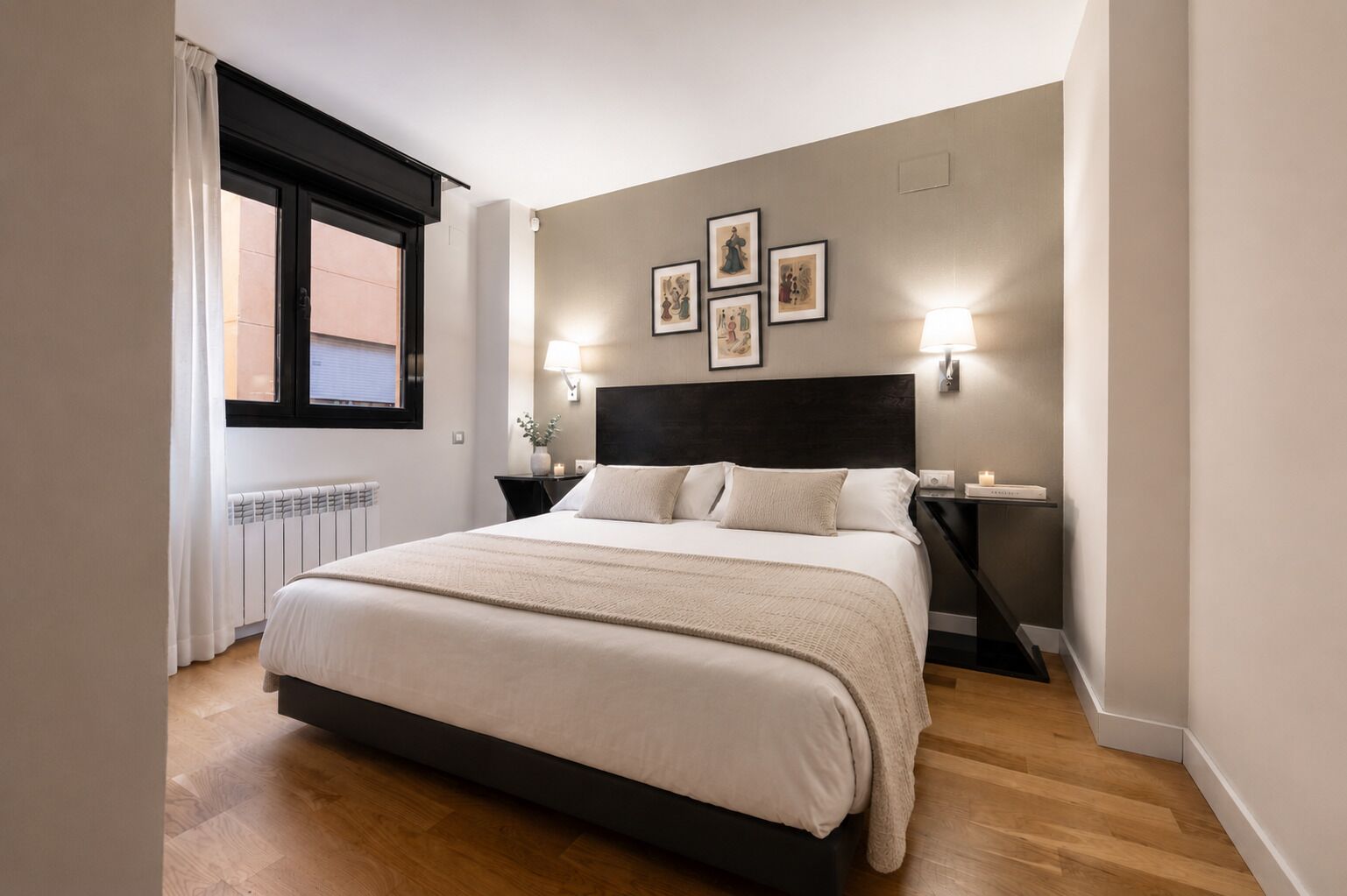 Une chambre à coucher avec un grand lit, des lampes de chevet, une fenêtre avec des rideaux et des tableaux encadrés accrochés au mur.