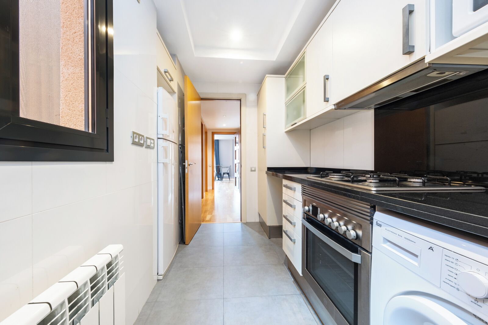 A narrow kitchen with white cabinets, a stove, and a washing machine.