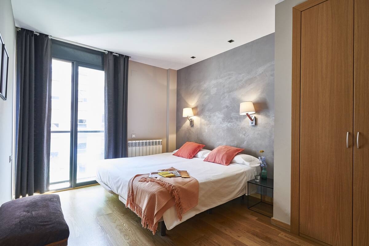 Een moderne hotelkamer met een groot bed, twee bedlampen, uitzicht door een schuifdeur en een houten garderobe.