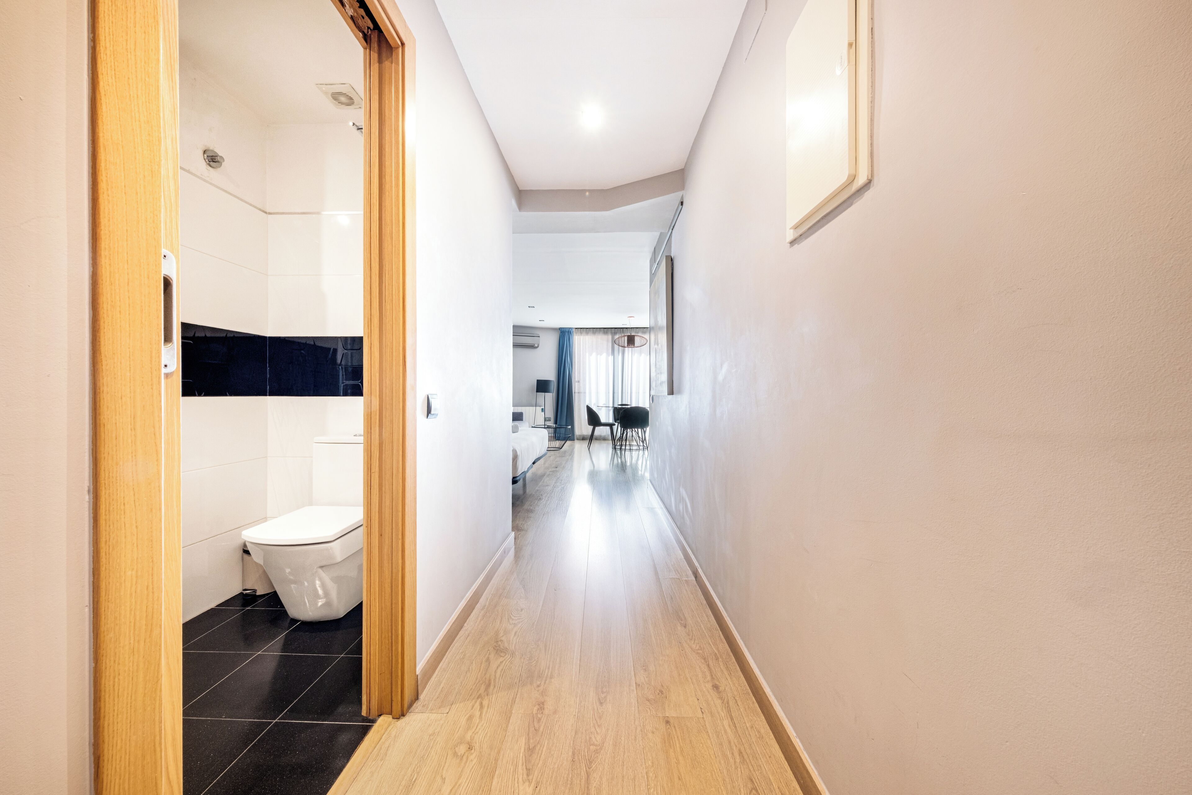 A modern hallway with a wooden floor, a white toilet, and a dining area in the background.