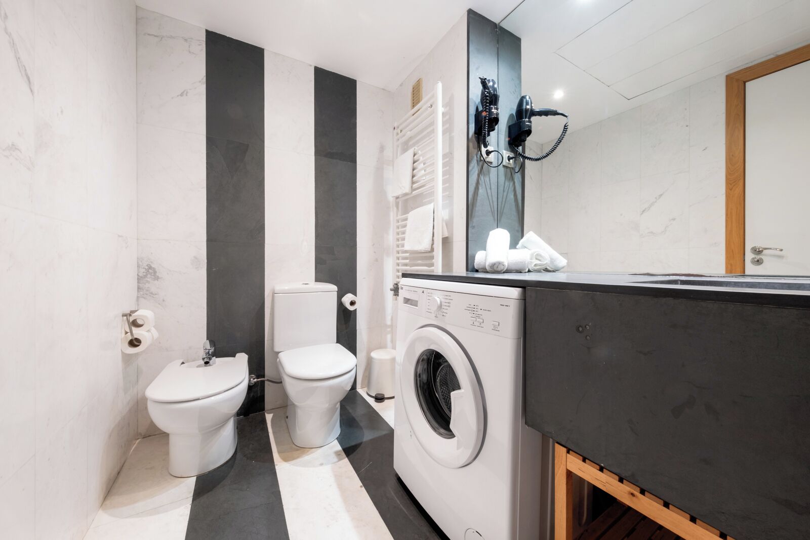 Ein kleines Badezimmer mit Waschmaschine, zwei Toiletten und einem Handtuchhalter.