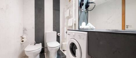 Ein kleines Badezimmer mit Waschmaschine, zwei Toiletten und einem Handtuchhalter.
