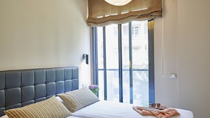 Un dormitorio con una cama grande, un cabecero oscuro y vistas a edificios desde la ventana.