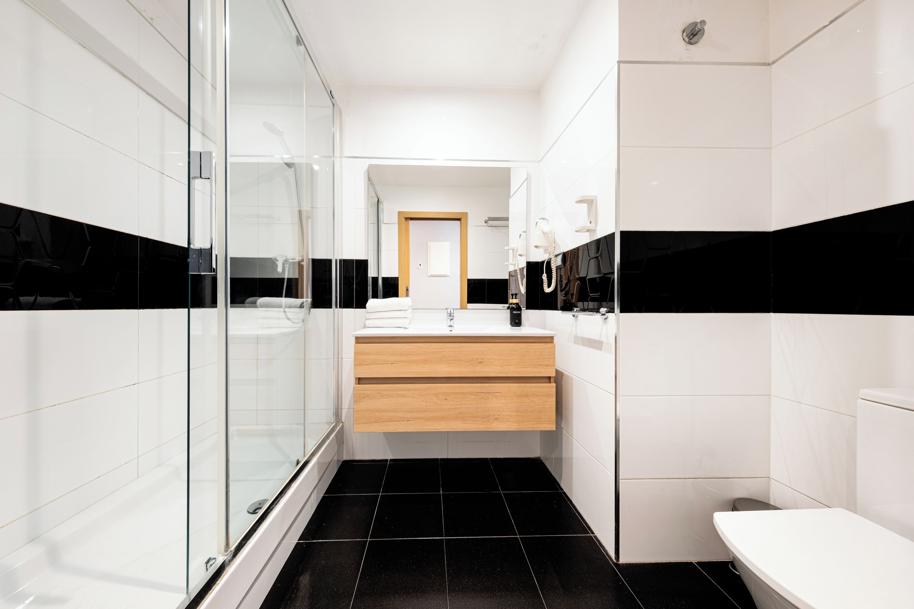 Een moderne badkamer met een douchecabine van glas, een houten wastafelmeubel en een wit toilet.
