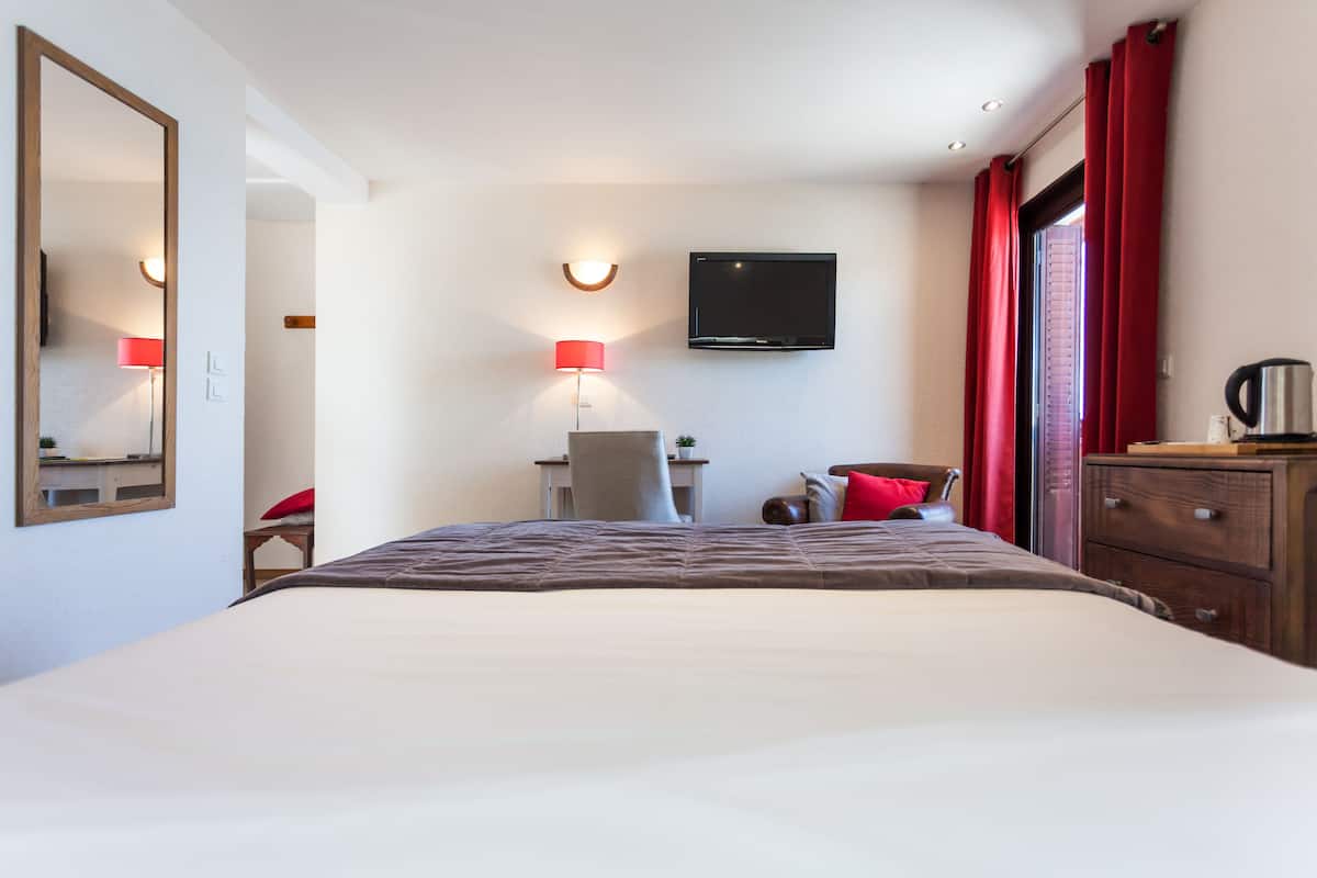 Una habitación de hotel con cama, escritorio, silla, televisor y cómoda.