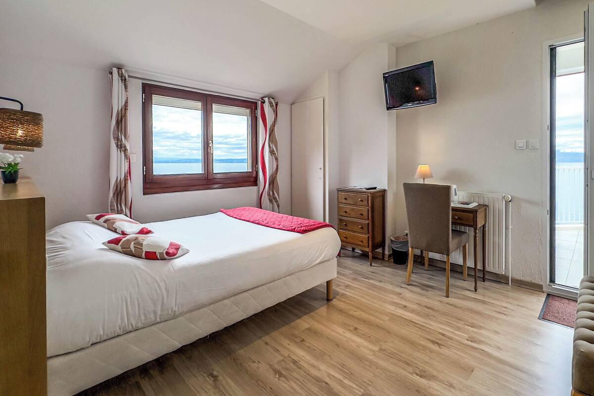 Un dormitorio con cama, escritorio, silla, televisor y vista al mar.