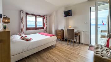 Quarto com cama, escrivaninha, cadeira, televisão e vista para o mar.