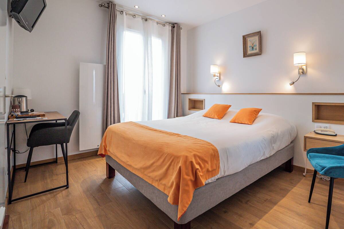 Una habitación de hotel con cama, escritorio, silla y mesita de noche.