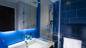 Une salle de bain moderne avec une douche à parois de verre, un lavabo blanc doté d’un distributeur de savon et une serviette suspendue à un porte-serviettes.