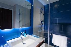 Une salle de bain moderne avec une douche à parois de verre, un lavabo blanc doté d’un distributeur de savon et une serviette suspendue à un porte-serviettes.