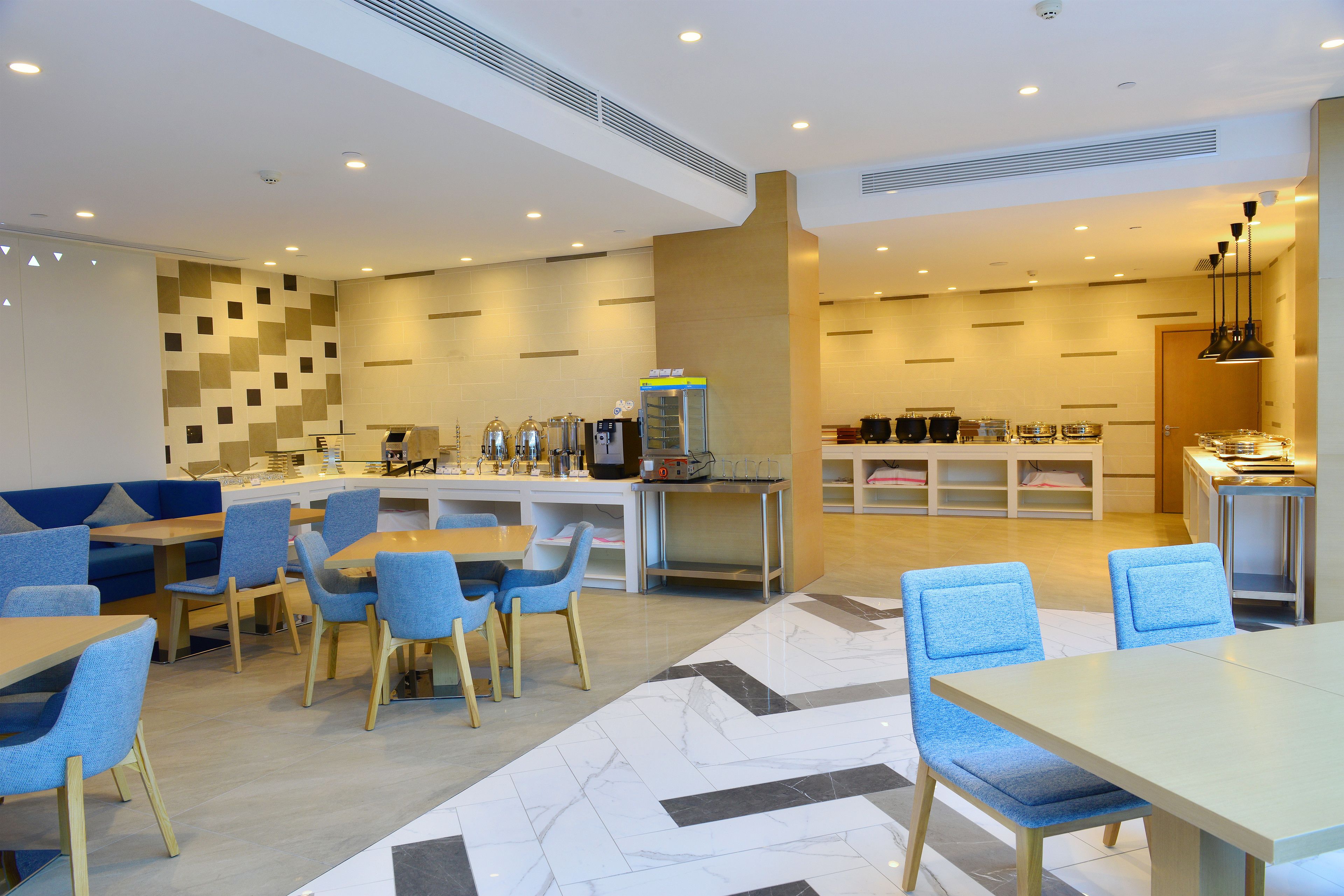 A modern hotel lobby with seating areas, a coffee station, and a counter with food options.