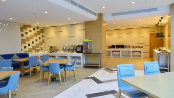 A modern hotel lobby with seating areas, a coffee station, and a counter with food options.