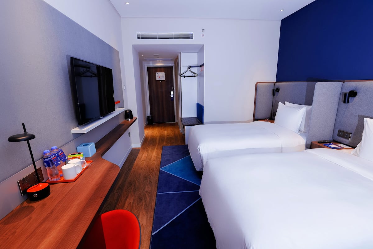 Une chambre d’hôtel avec deux lits, un bureau doté d’un téléviseur à écran plat, une chaise rouge et un tapis bleu.