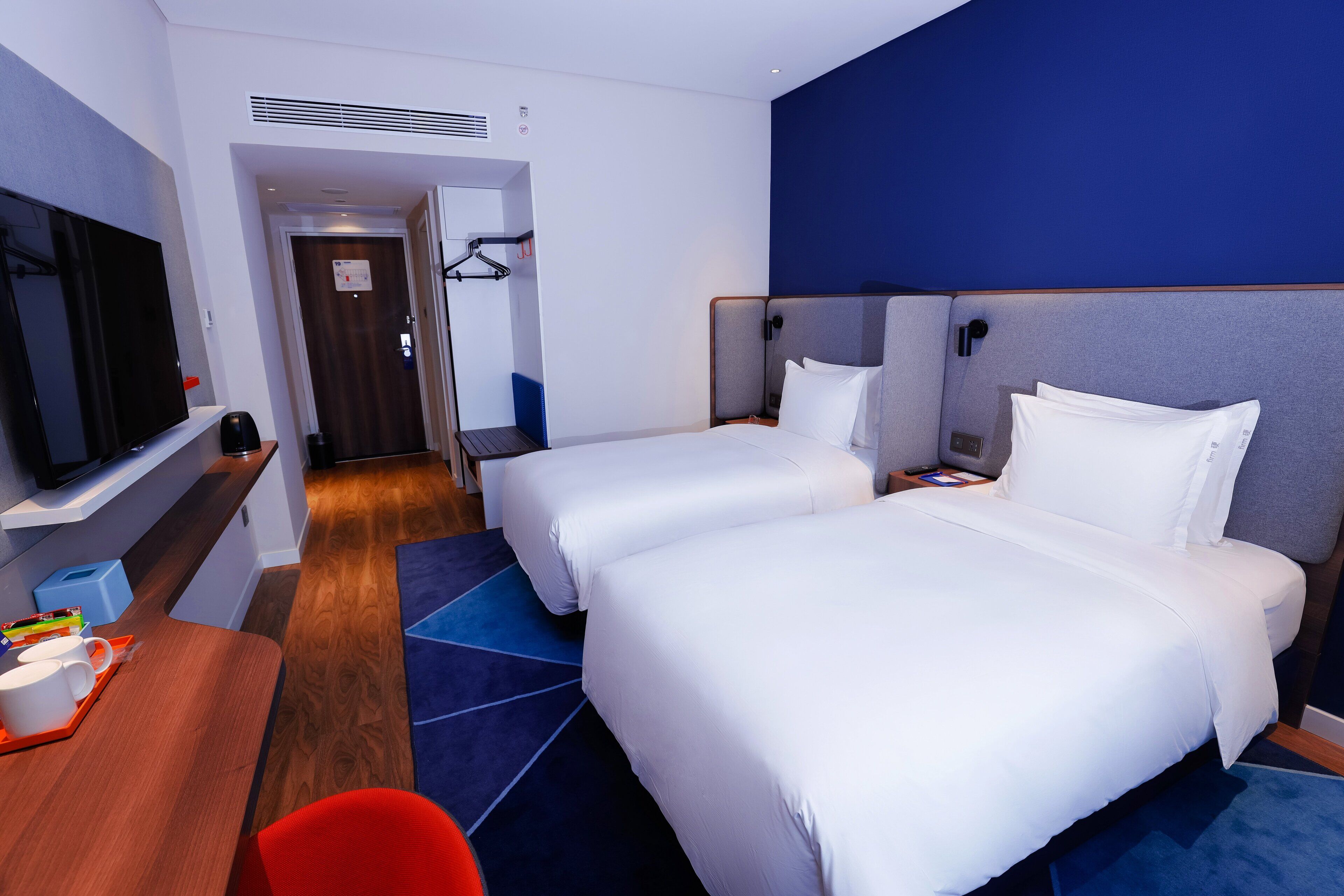 A hotel room with two beds, a TV, a desk with a tray of items, and a red chair.